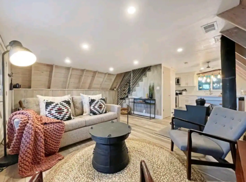 Cozy living room with a sofa, patterned pillows, a coffee table, and warm lighting, featuring a rustic design.